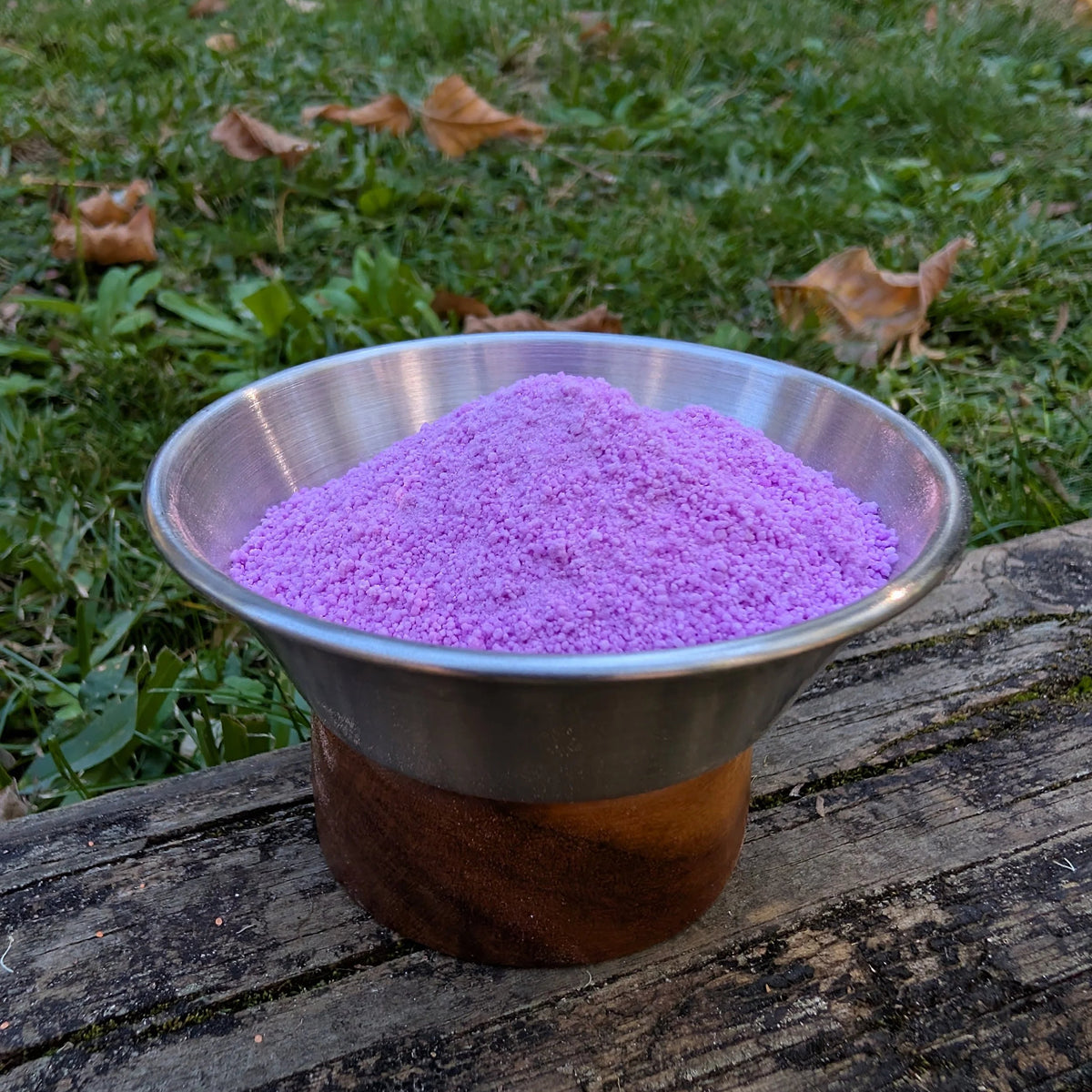Bowl of Wisteria Hex purple fizzy powder on a log