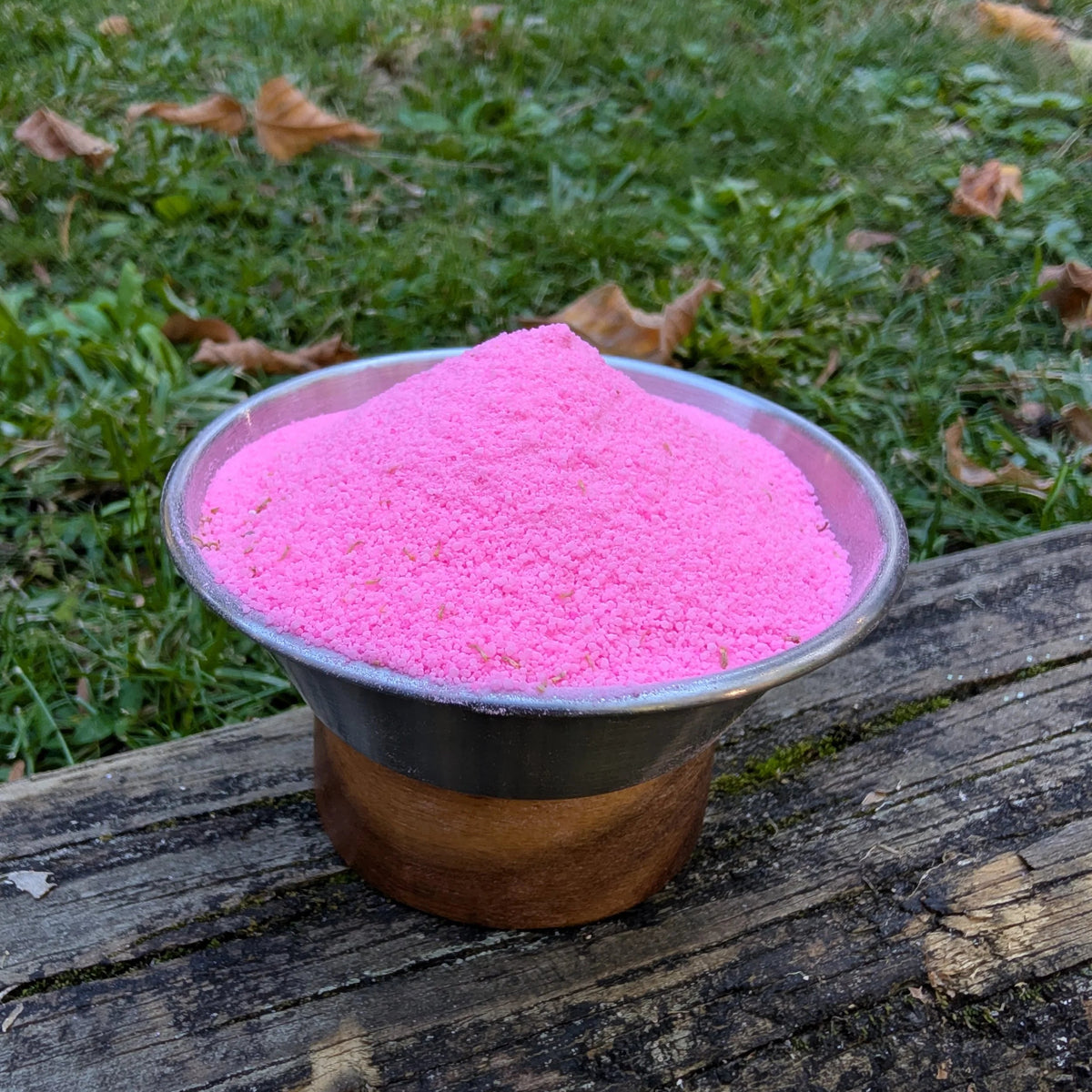 Bowl of Flamingo Spell hot pink fizzy powder on a log