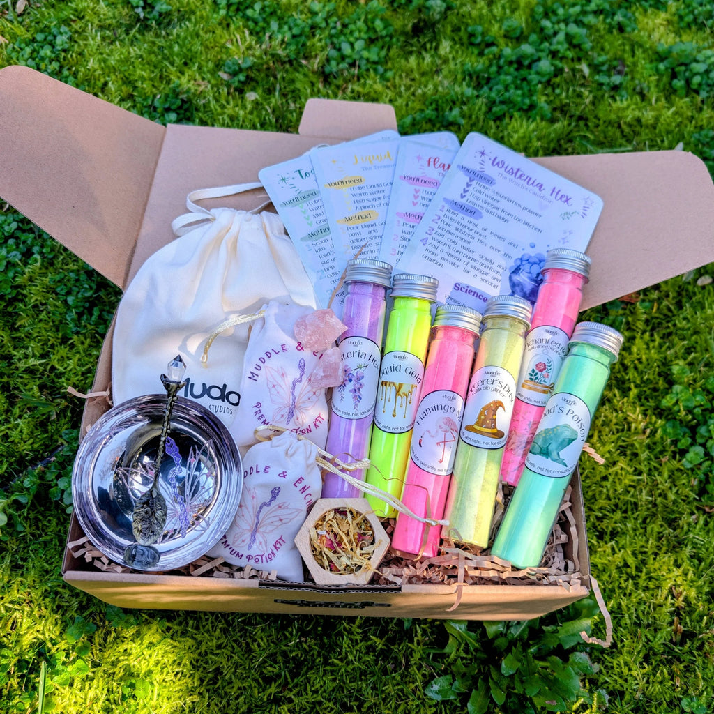 Open Muddle & Enchant kit box with a drawstring bag, steel bowl, test tubes and story cards, on grass