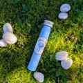 Standard test tube of blue fizzy powder with a trident label, on grass among white stones