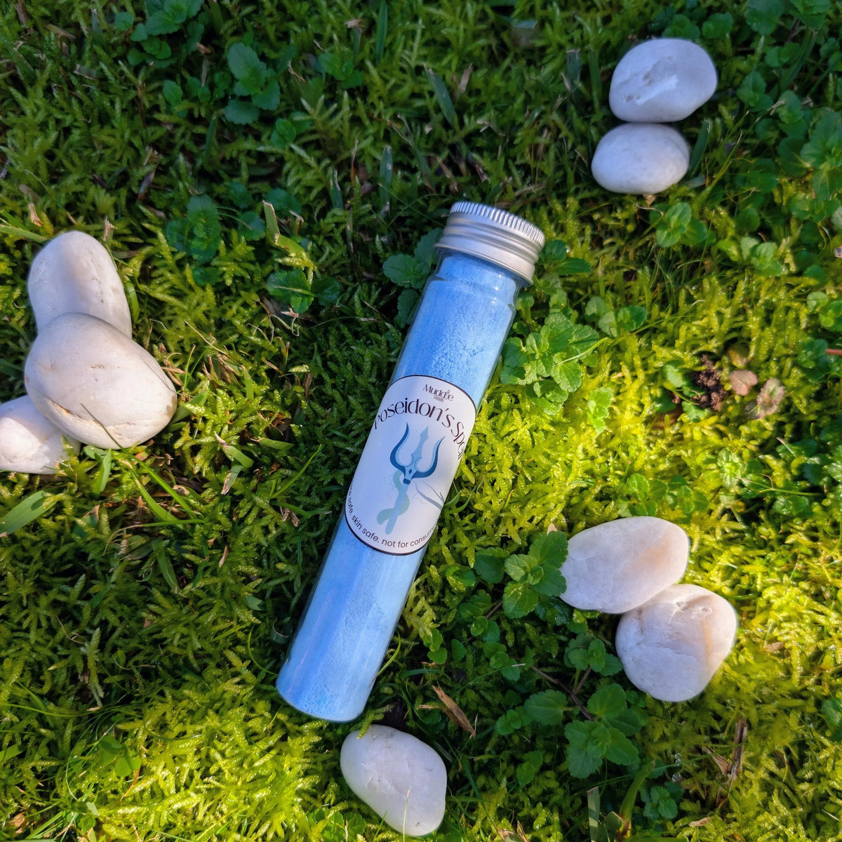 Standard test tube of blue fizzy powder with a trident label, on grass among white stones