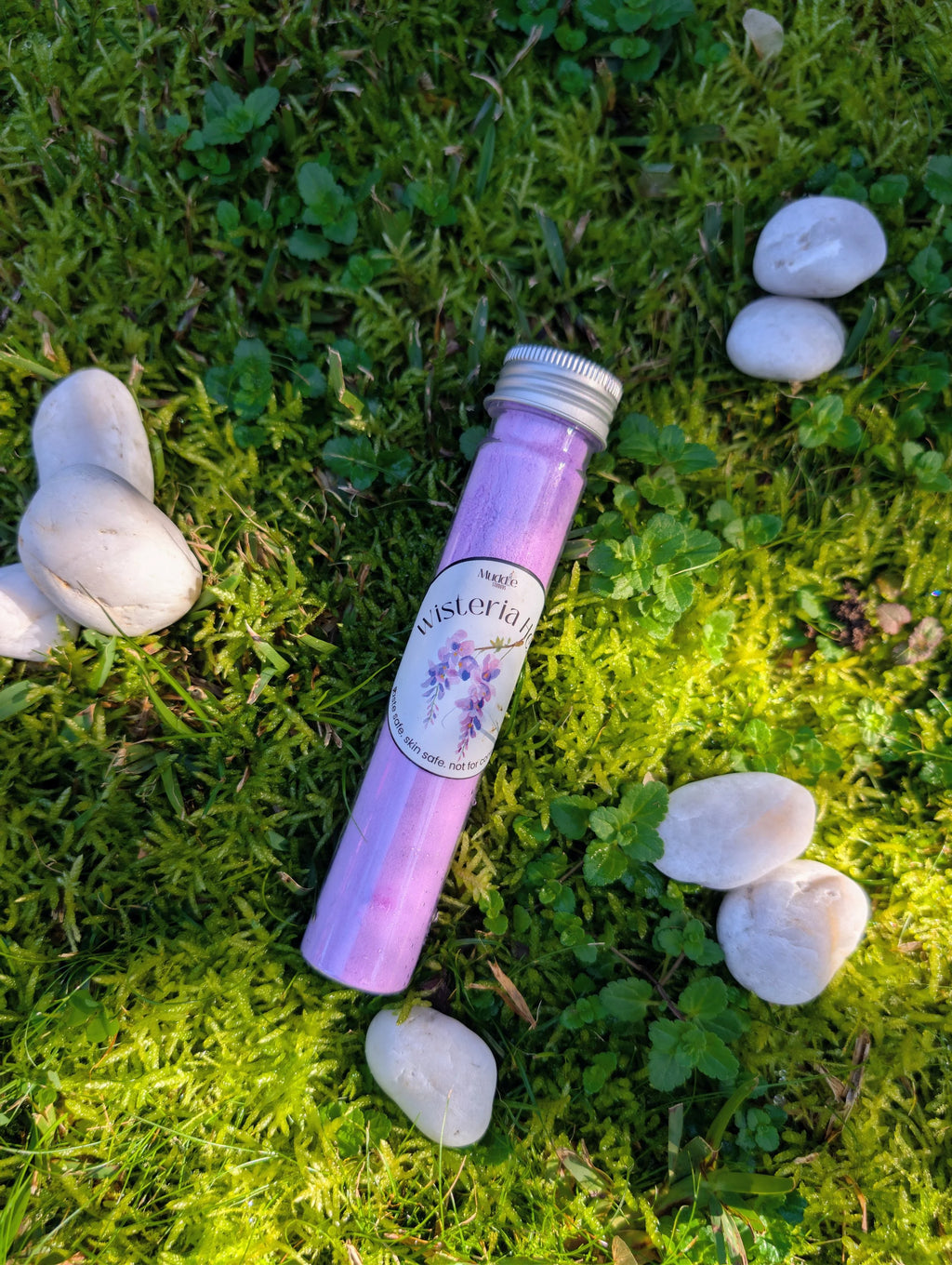 Standard test tube of purple fizzy powder on grass among white stones