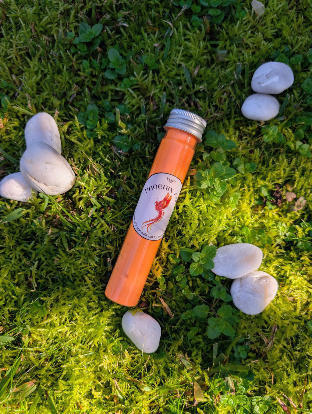 Standard test tube of orange fizzy powder on grass among white stones