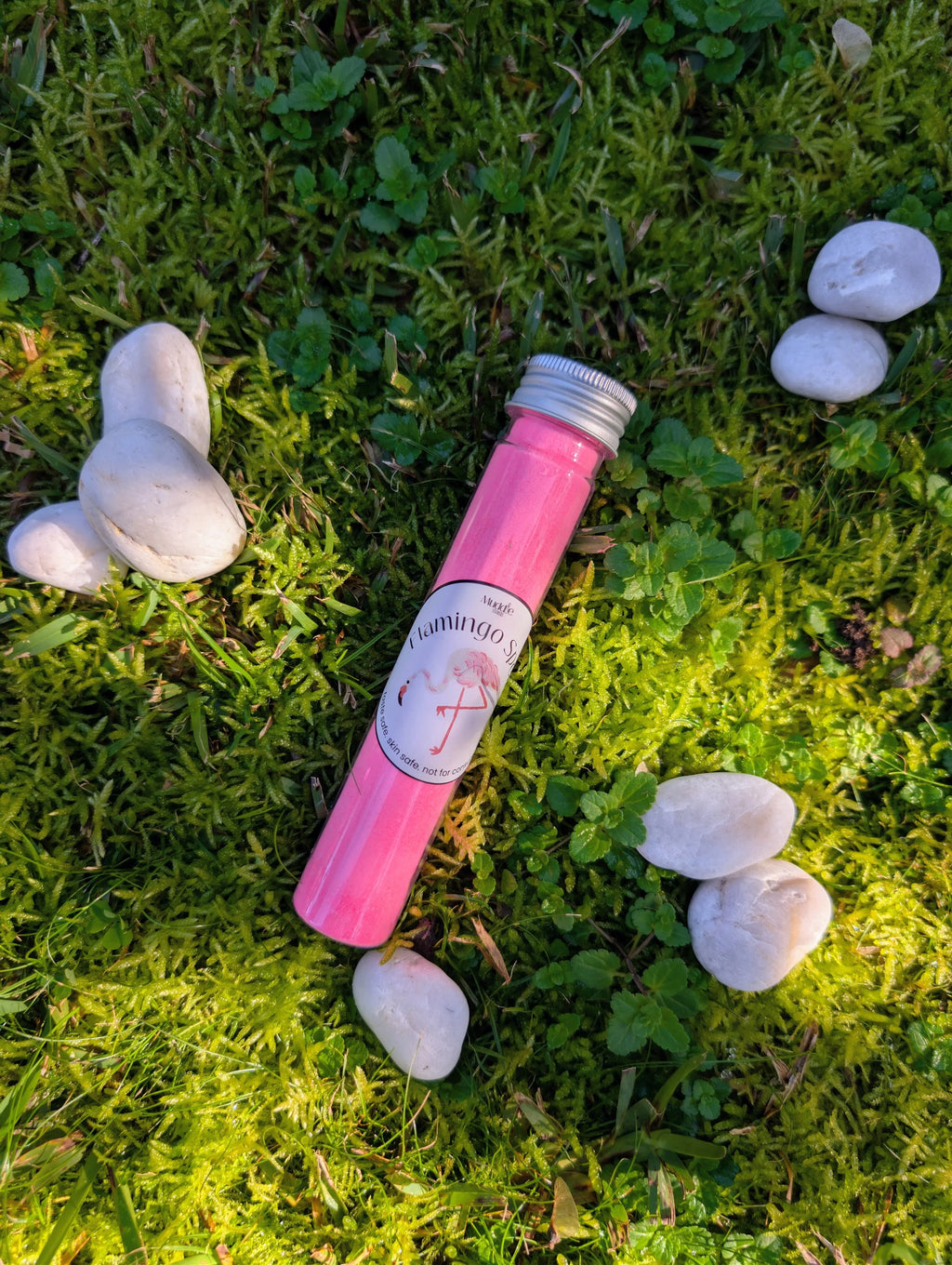 Standard test tube of pink fizzy powder on grass among white stones