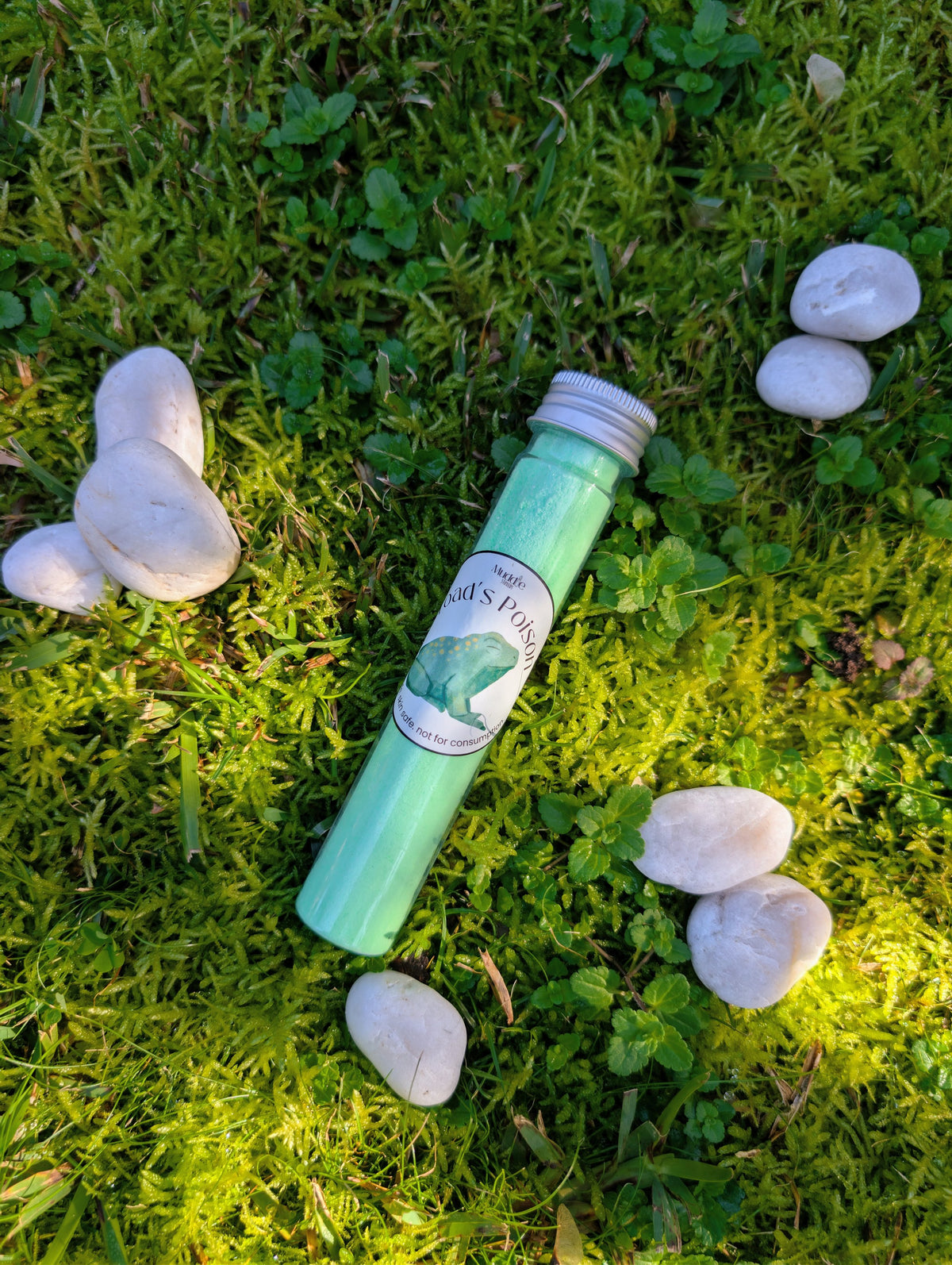 Standard test tube of teal fizzy powder on grass among white stones