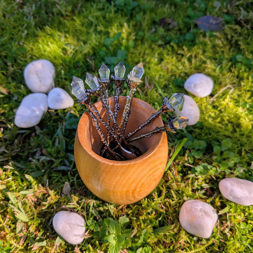 Crystal-topped teaspoons standing in a wooden cup on grass among white stones