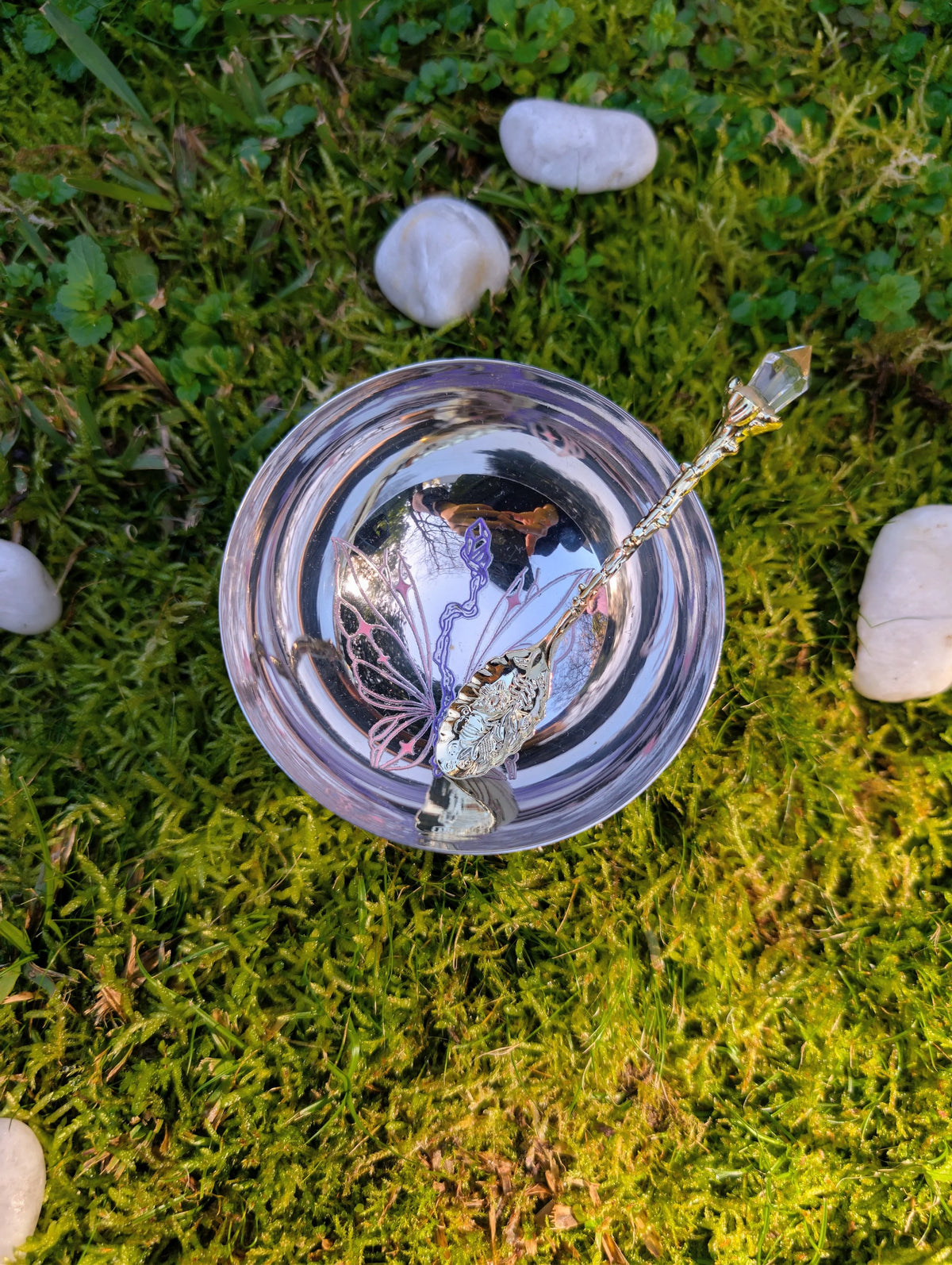 Stainless steel bowl and spoon seen from above on moss and white stones