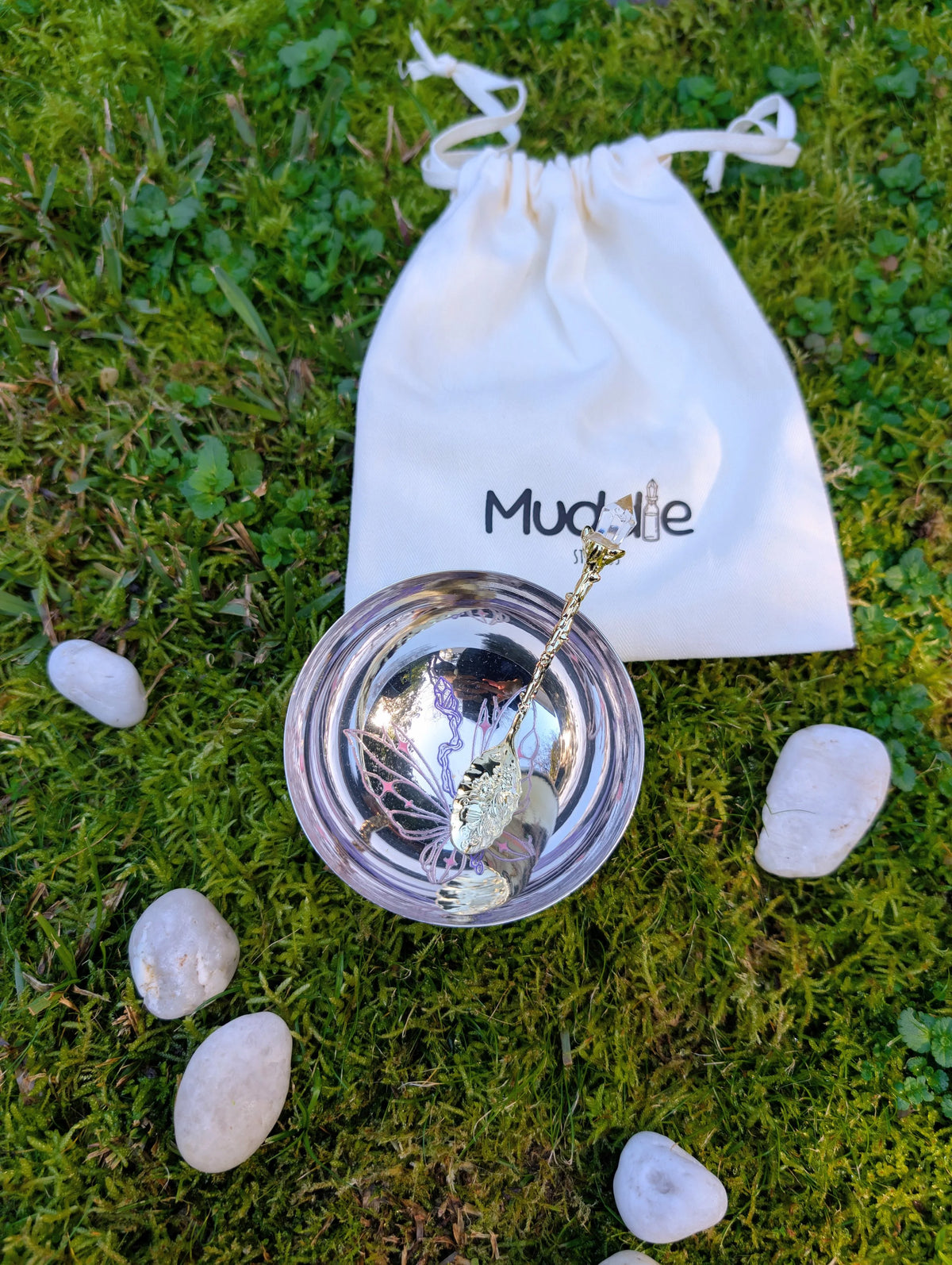 Stainless steel bowl and spoon with a Muddle Studios drawstring bag behind, on moss 