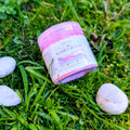Sunset Bloom fizzy powder jar with a pink lid on grass beside white stones