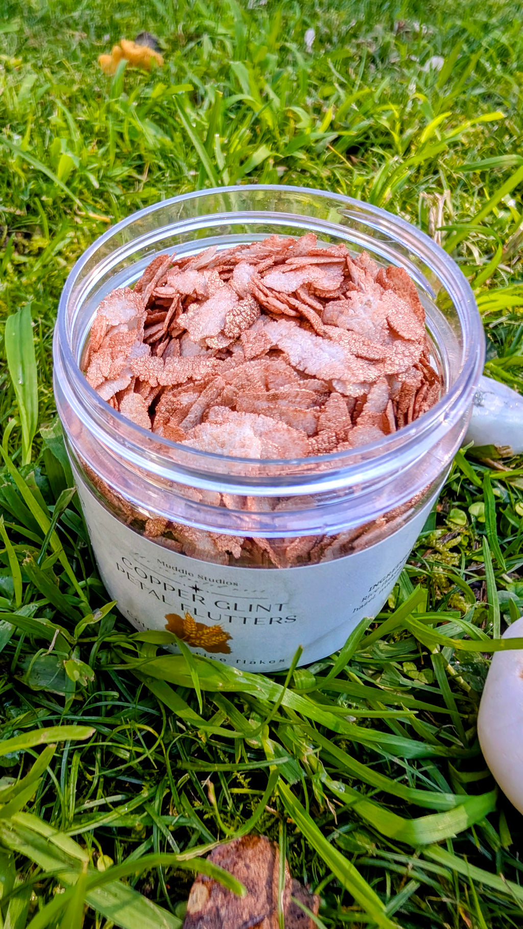 Open jar of Copper Glint Petal Flutters, copper-coloured rice flakes, close up