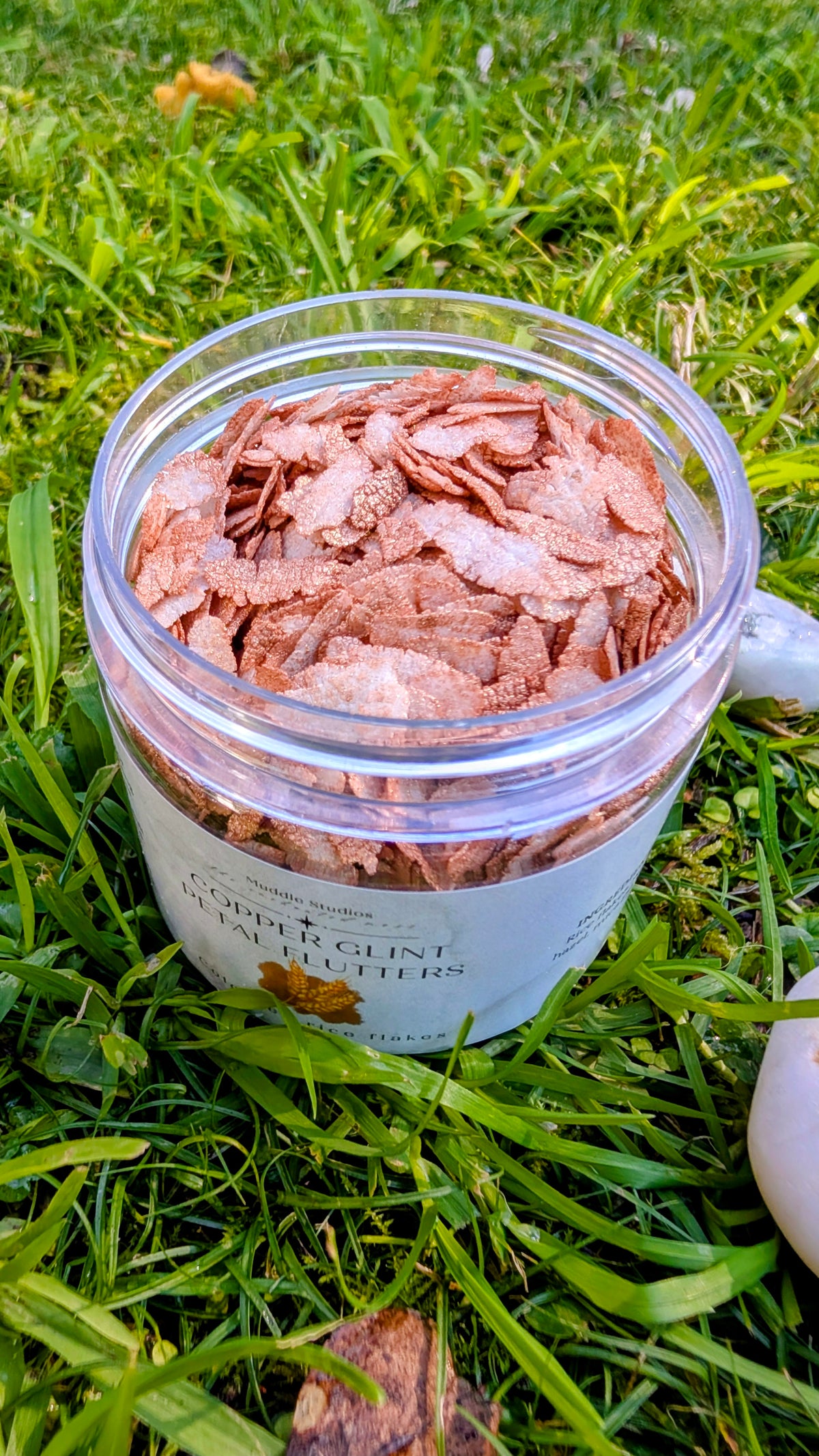 Open jar of Copper Glint Petal Flutters, copper-coloured rice flakes, close up