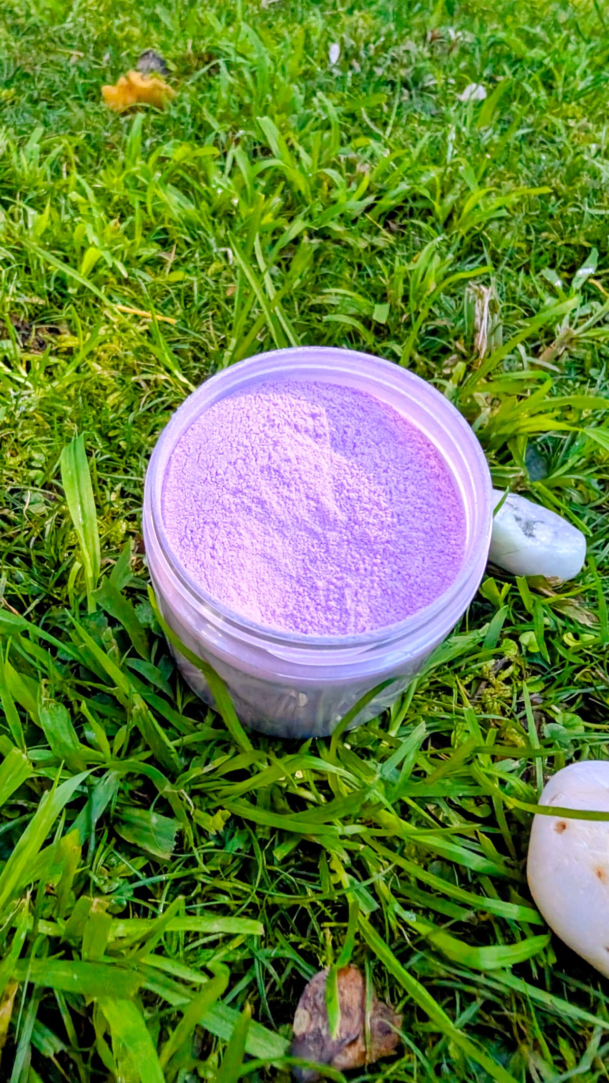 Open jar of Quiet Bloom, soft purple fizzy powder, seen from above on grass