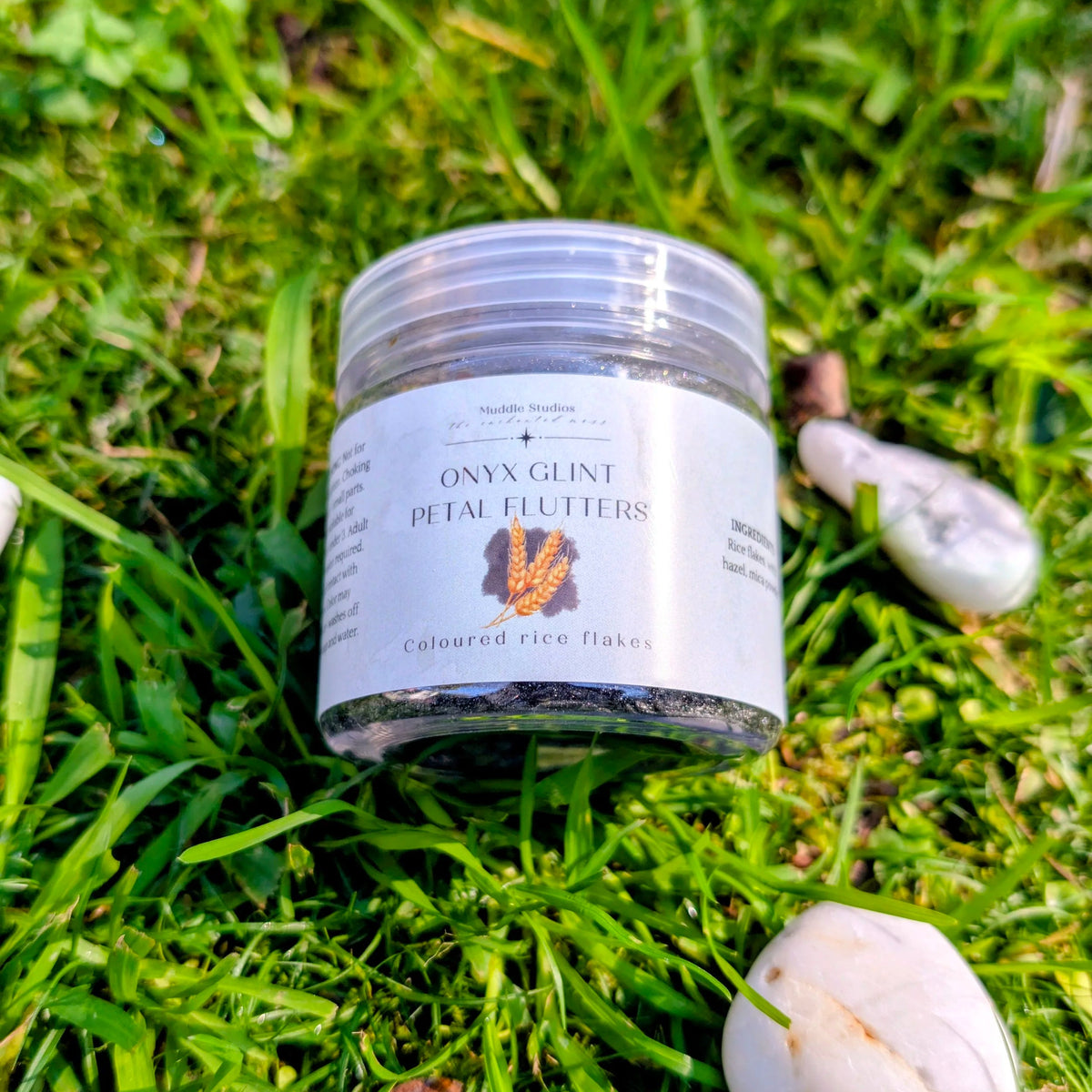 Onyx Glint Petal Flutters jar on grass beside white stones