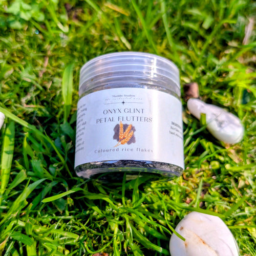 Onyx Glint Petal Flutters jar on grass beside white stones