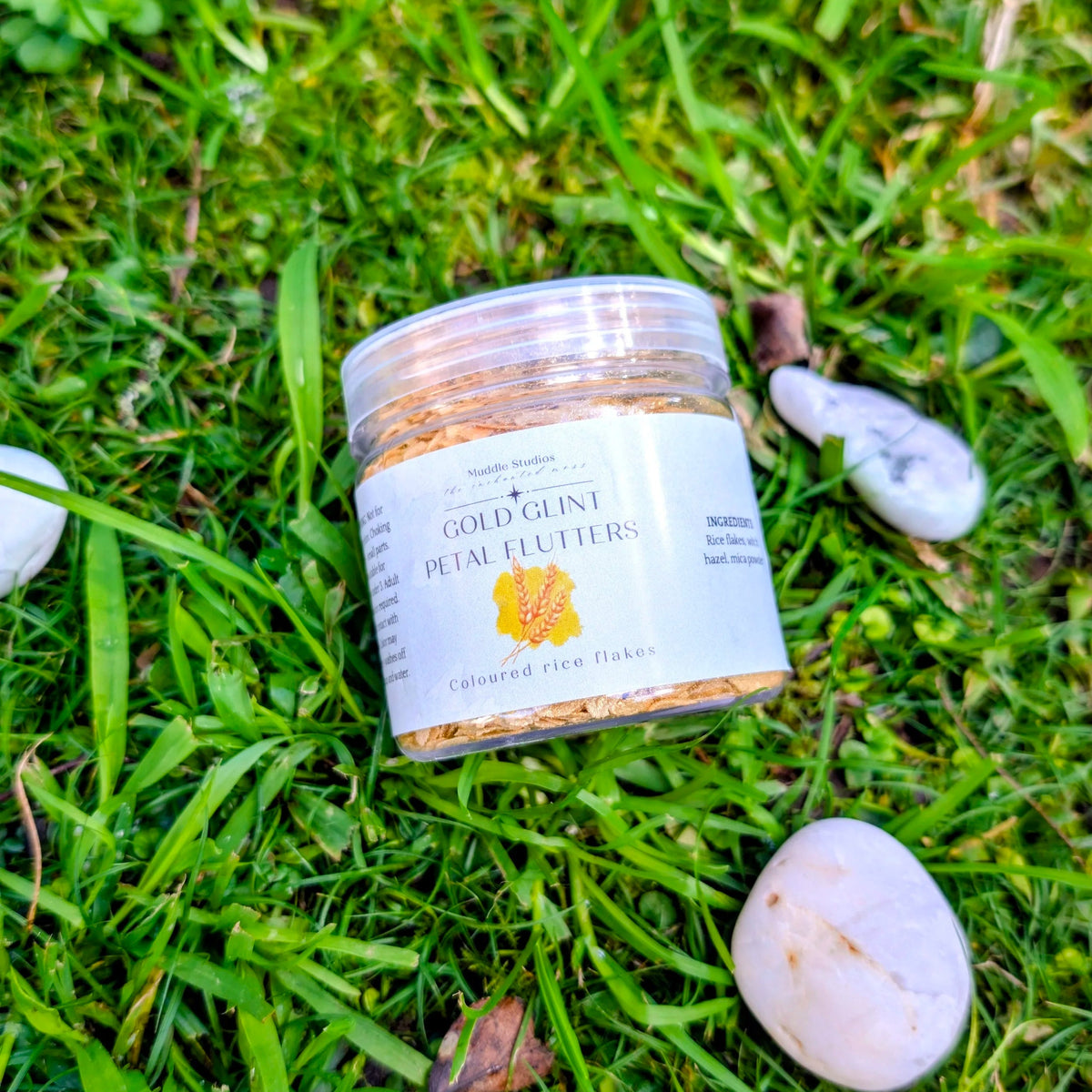 Copper Glint Petal Flutters jar with an orange label on grass beside white stones