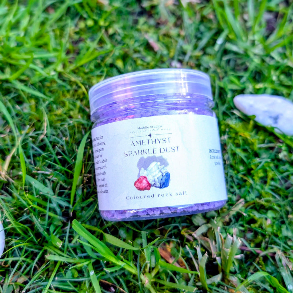 Amethyst Sparkle Dust jar filled with purple crystals, on grass beside white stones
