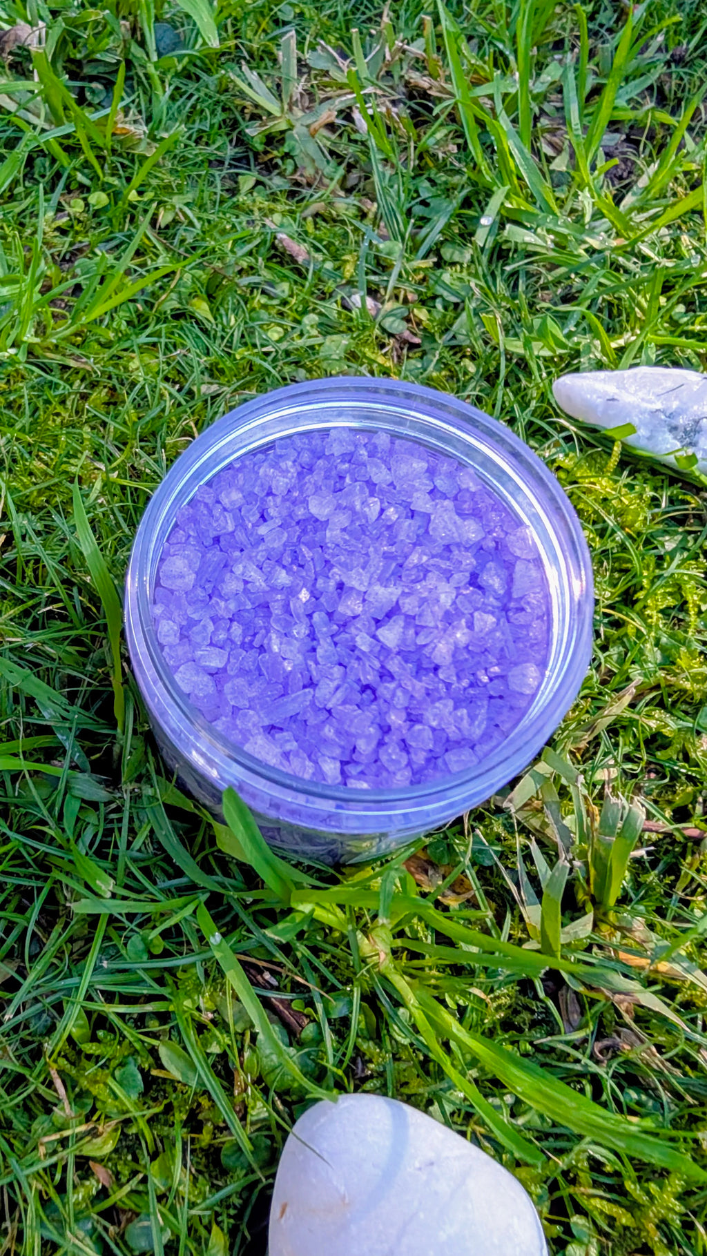 Open jar of Amethyst Sparkle Dust, purple mica-coated rock salt crystals, seen from above on grass