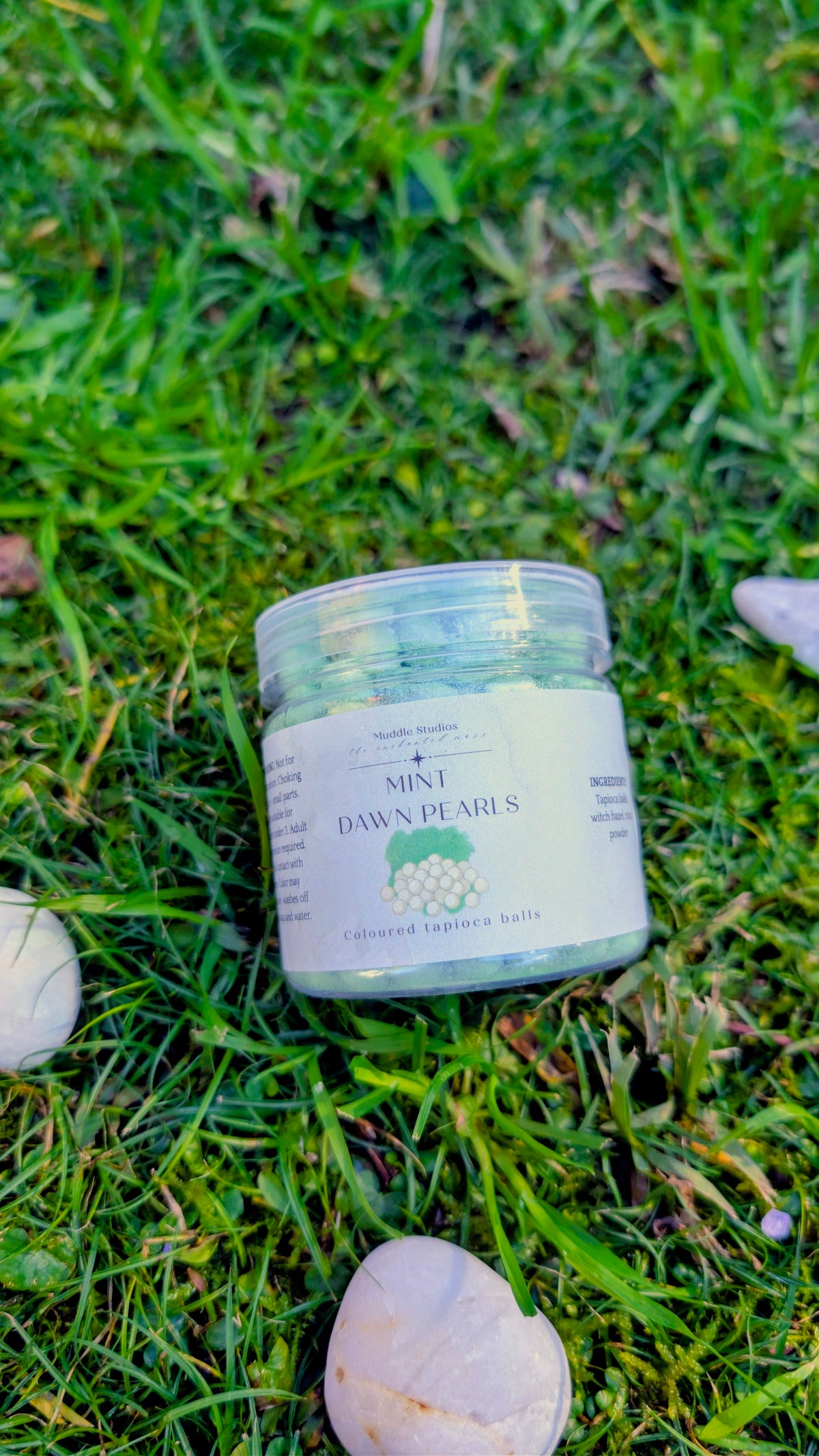 Mint Dawn Pearls jar with a mint green label on grass beside a stone 