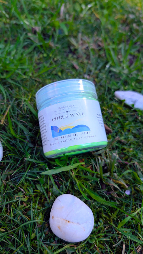 Citrus Wave fizzy powder jar with a blue wave label on grass beside a white stone 