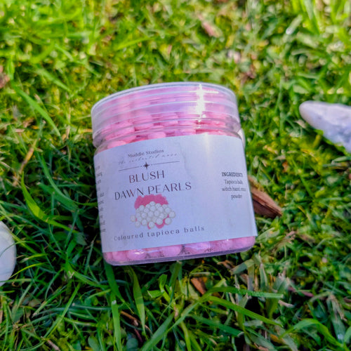 Blush Dawn Pearls jar with a pink label on grass beside white stones