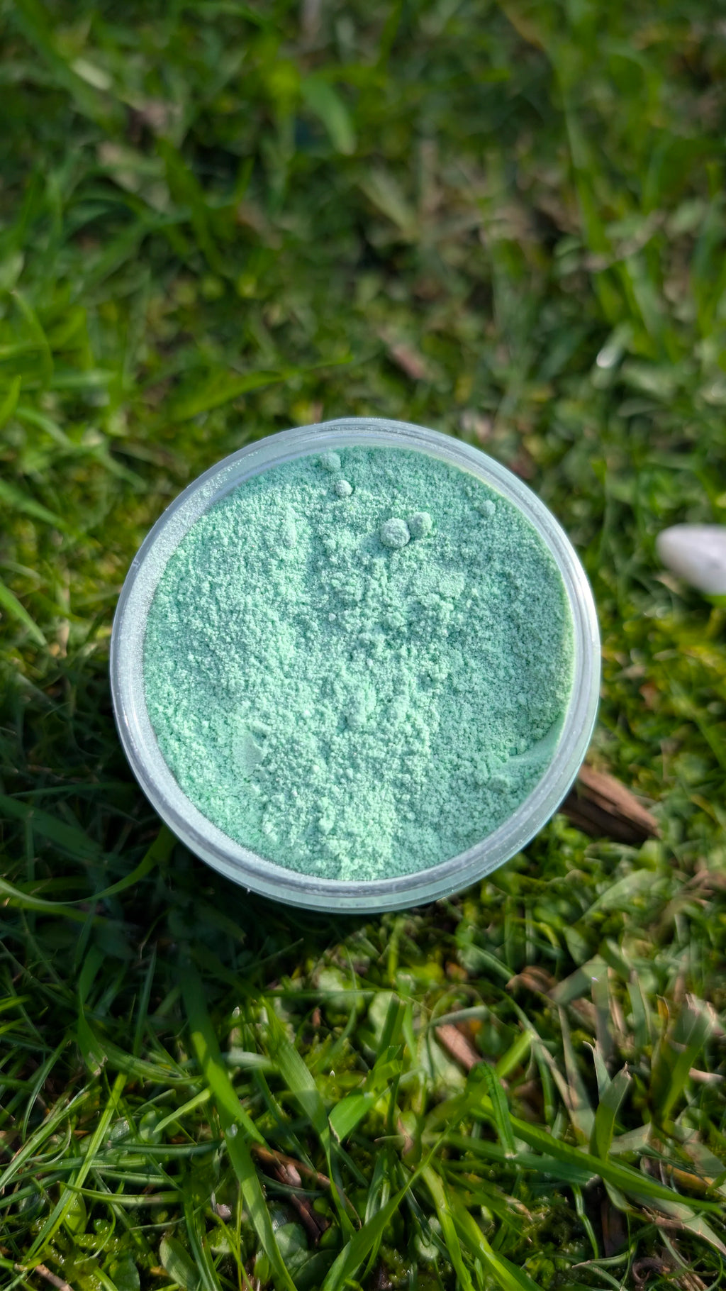 Open jar of Minty Hush, pastel green fizzy powder, seen from above on grass 