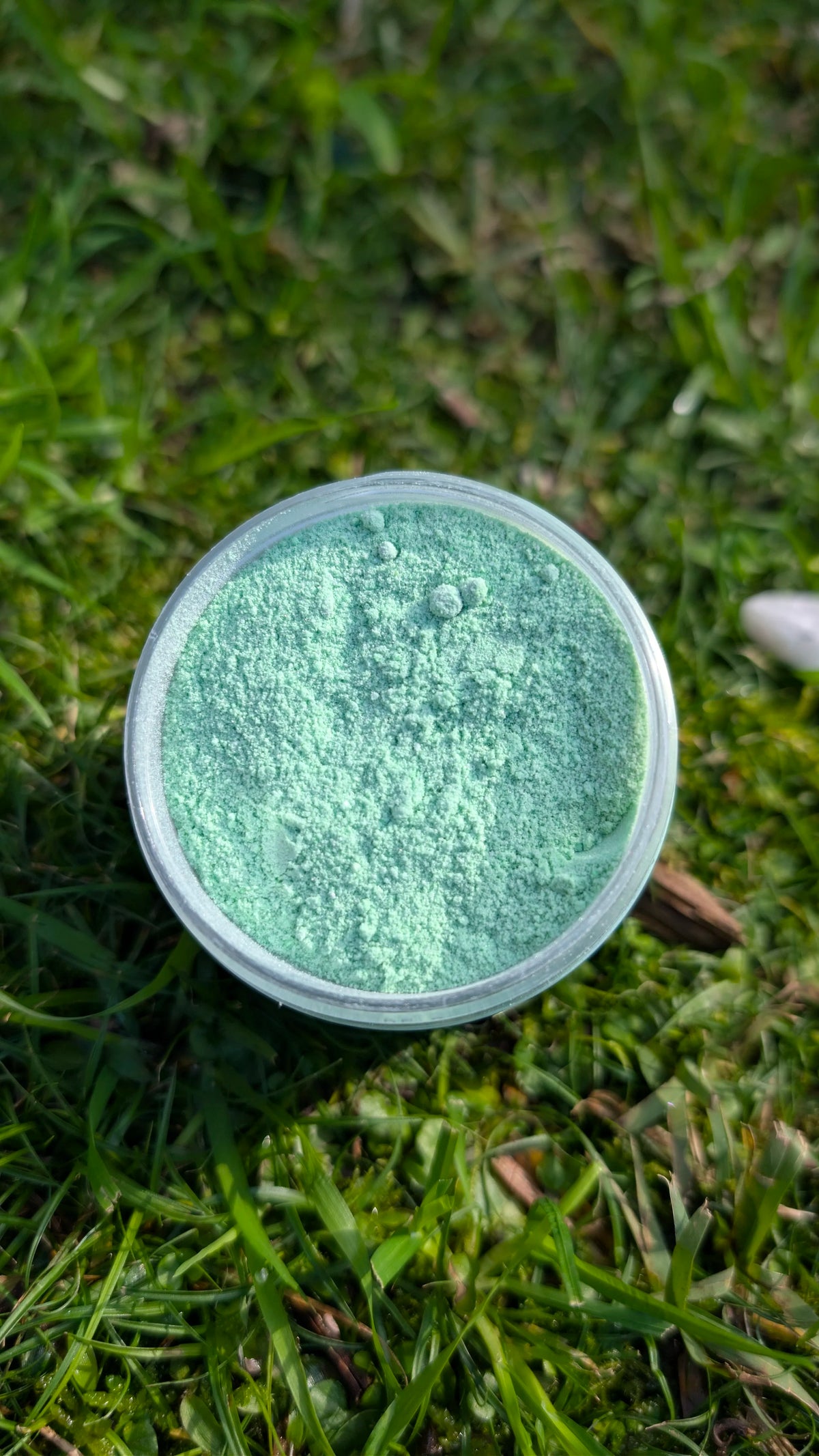 Open jar of Minty Hush, pastel green fizzy powder, seen from above on grass 