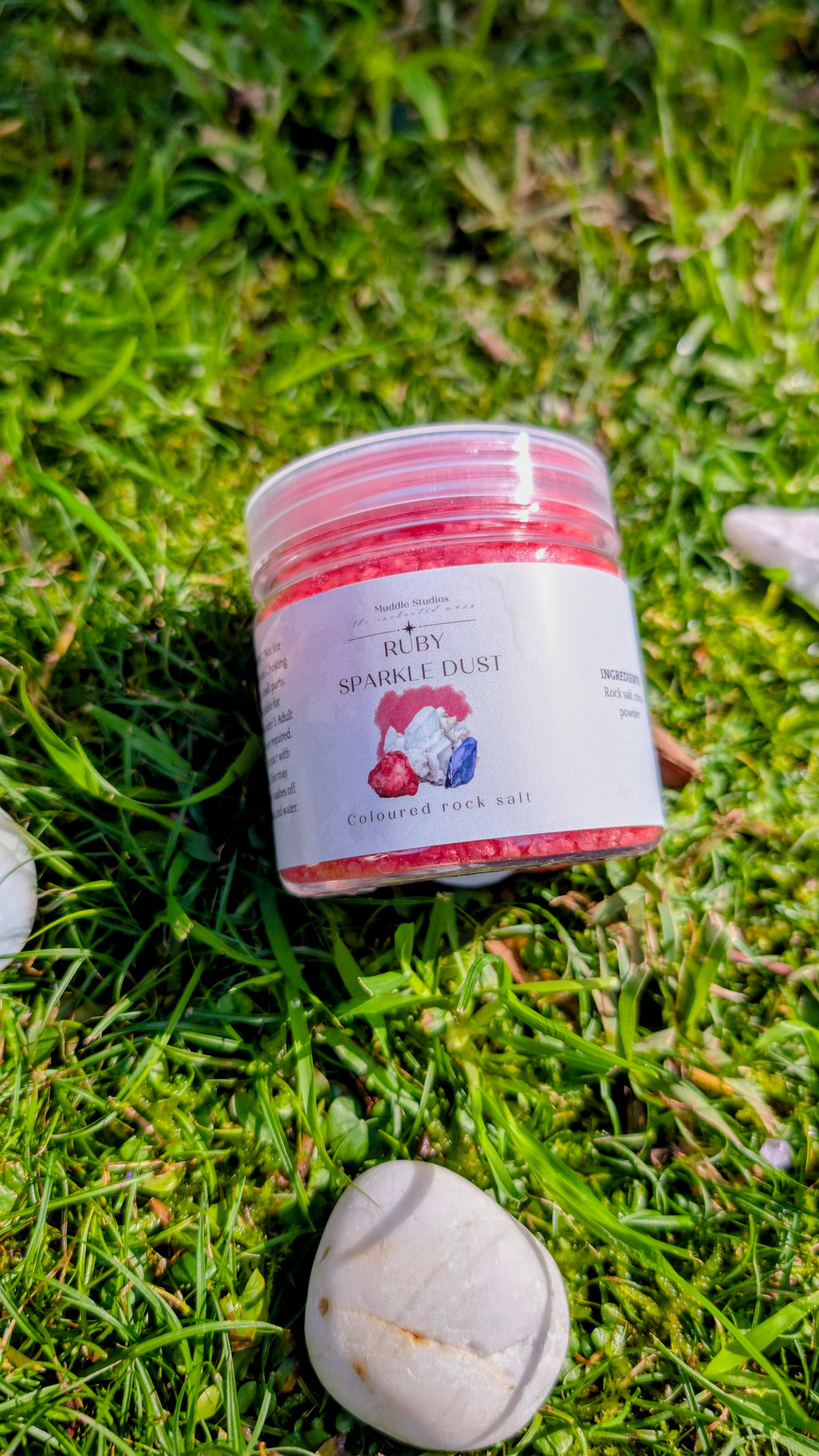 Ruby Sparkle Dust jar with a red label on grass beside a stone