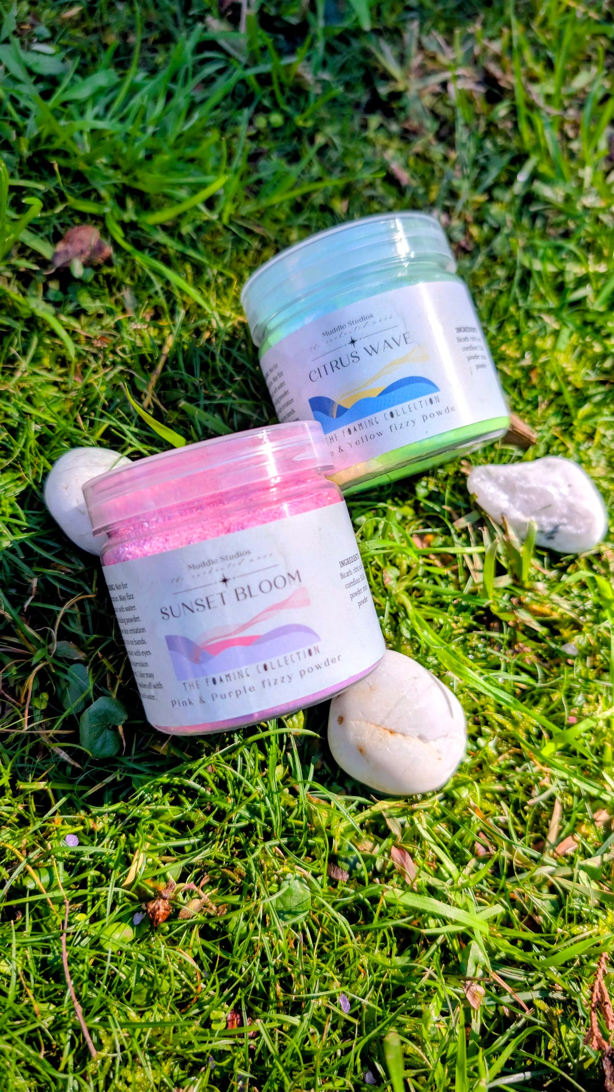 Sunset Bloom and Citrus Wave fizzy powder jars side by side on grass