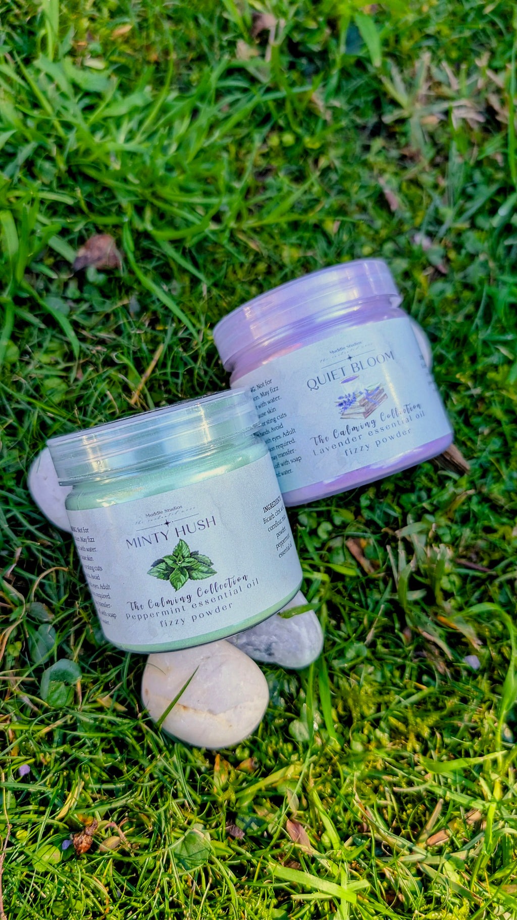 Quiet Bloom and Minty Hush fizzy powder jars side by side on grass with a white stone 