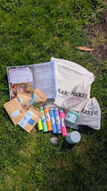The Root & Bloom Kit laid out on grass with an open storybook, a drawstring Muddle bag, colourful test tubes, a jar and pouches