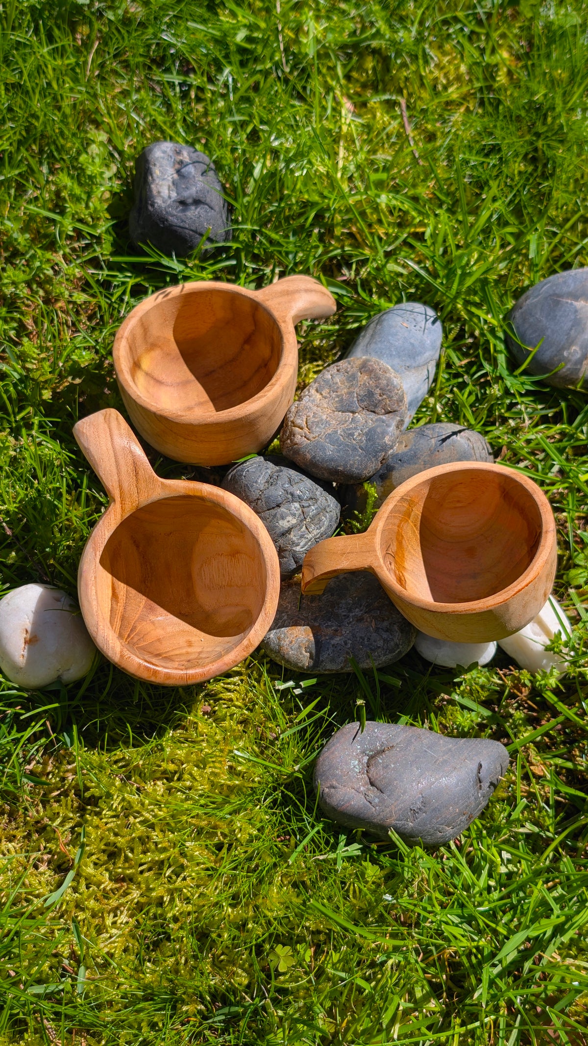 Three small wooden Papoose baby cups on grass among stones