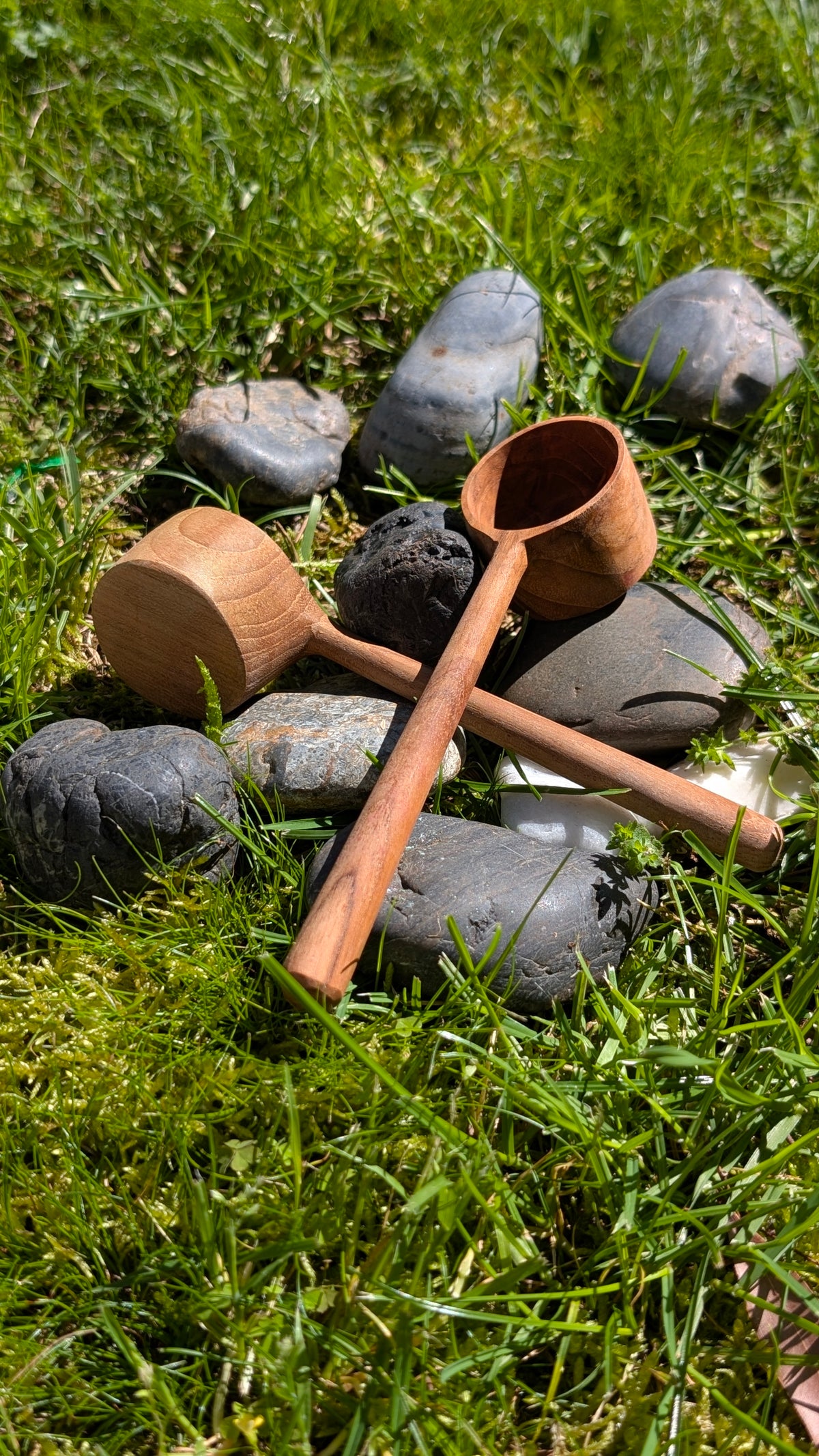 Small wooden pot and scoop on grass among dark stones
