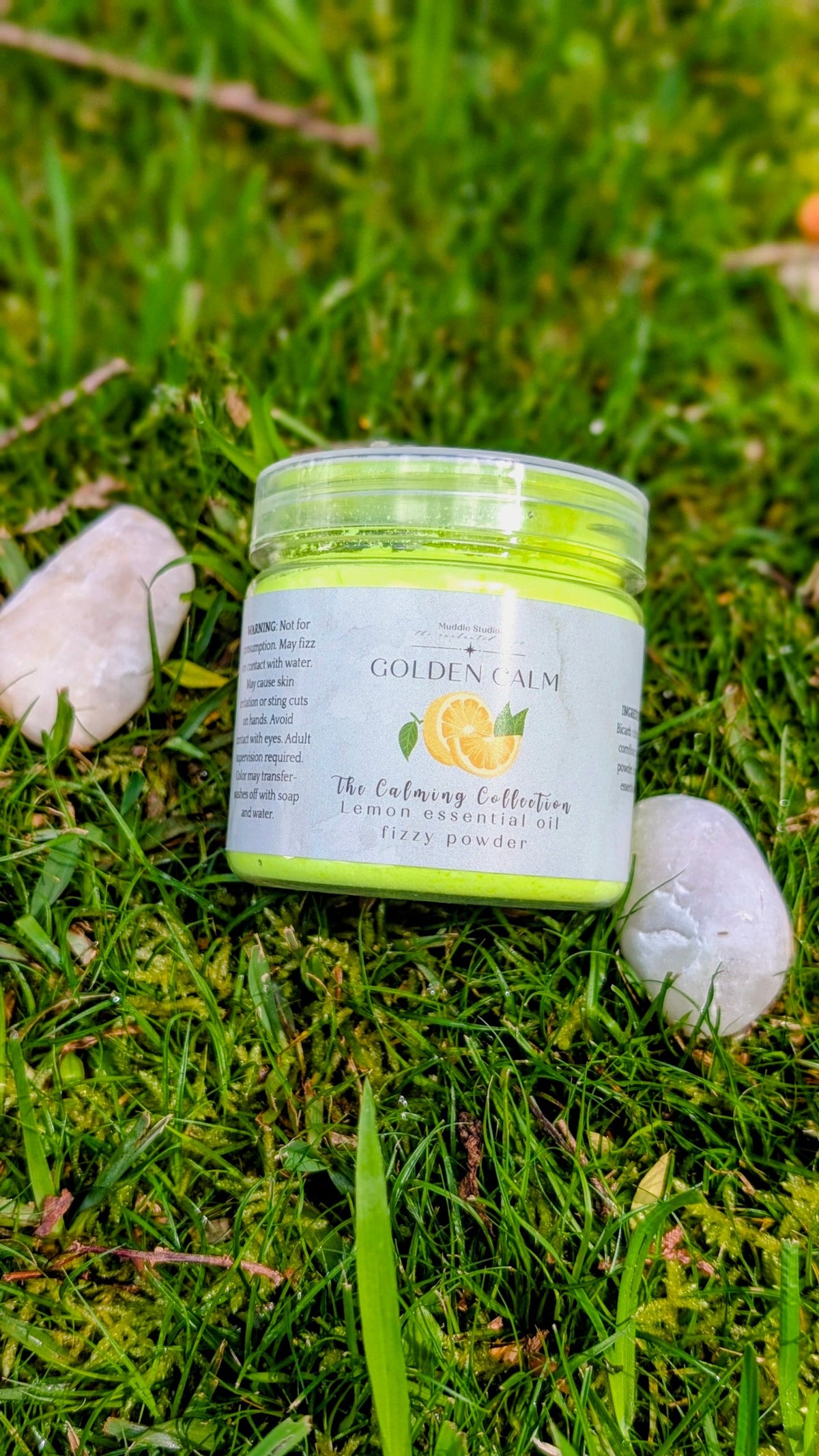 Golden Calm lemon fizzy powder in a 150ml jar with a lemon label, on grass beside two white stones
